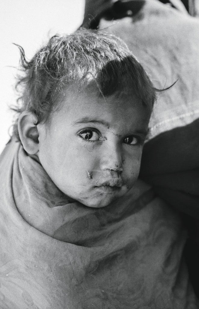 Podría ser un niño de cualquier guerra, da igual un sitio que otro. Sujeto a la espalda de su madre, mira, con la serenidad de quien ya ha visto demasiado, al extraño que se acerca con una cámara y se arrodilla a su lado para enfocar. Todo está ahí, pues lo más terrible de una guerra, o al menos lo que recuerdas con más exactitud pasados los años, no son los muertos y la destrucción, sino la mirada de los niños. La de éste es un buen resumen de todo. Si amplío mucho la imagen, puedo verme a mí mismo en el momento de tomar la foto, reflejado en sus pupilas oscuras. No es un buen sitio para verse.