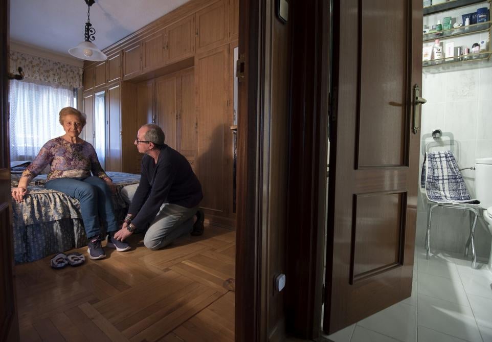 Julio ayuda a calzarse las zapatillas a su madre Pilar en el dormitorio del piso que comparten.