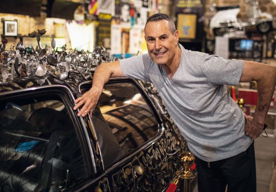 Uri Geller en su museo de Tel Aviv, en Israel, junto a un Cadillac con miles de cucharas dobladas por él a lo largo de los años. Su buen aspecto físico lo atribuye a la ingesta diaria de vitaminas en pastillas.