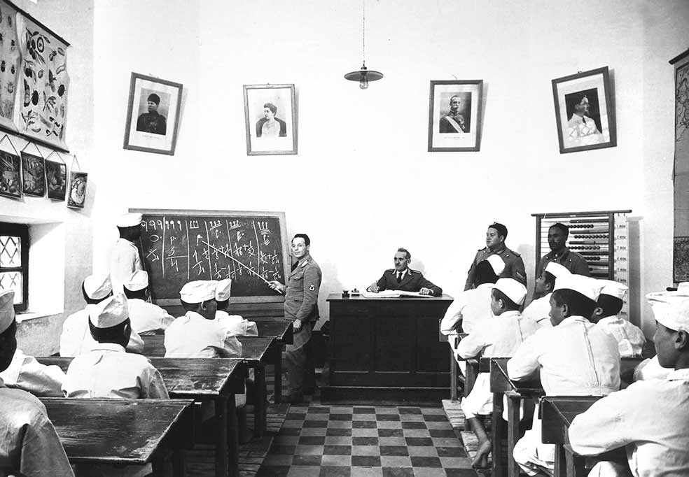 Año 1923, un aula escolar en Trípoli. Un militar italiano imparte las clases a los jóvenes libios. De las paredes cuelgan retratos de sus nuevos próceres. Entre ellos, Mussolini.