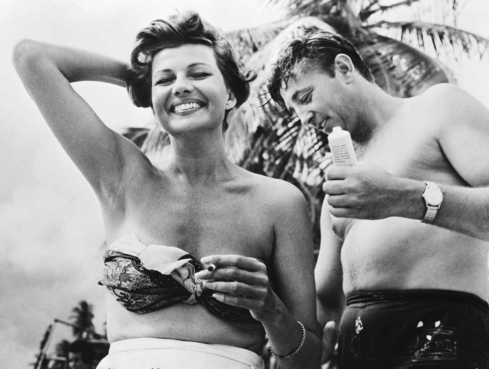 Robert Mitchum le pone crema en una playa de Trinidad donde rodaban Fuego escondido, en 1957. Rita era una superestrella.