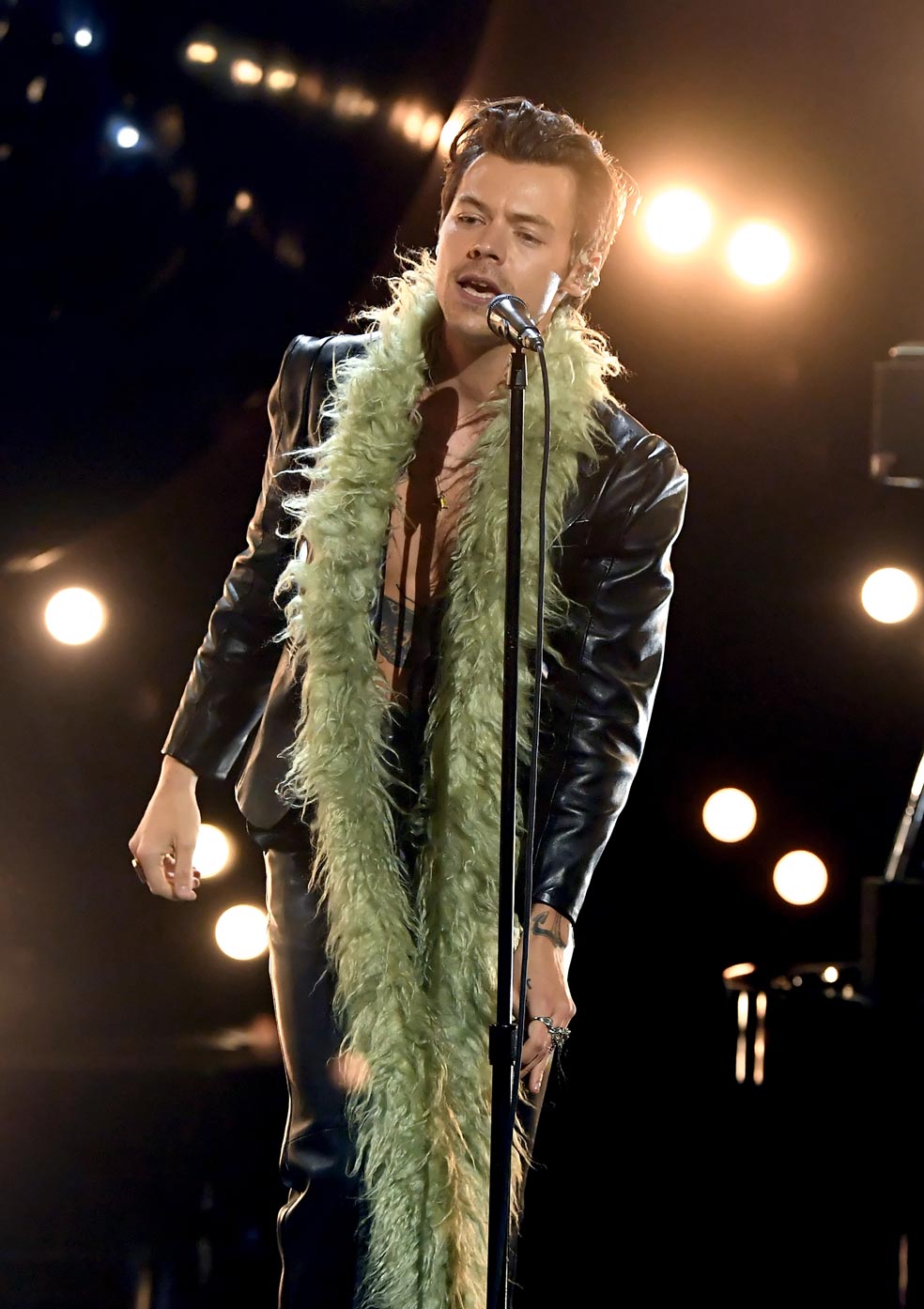 Harry Styles se subió al escenario de los premios Grammy 2021 con un traje de cuero negro, con pantalón de tiro algo y chaqueta desabrochada, al que sumó una boa verde y unos zapatos de plataforma.