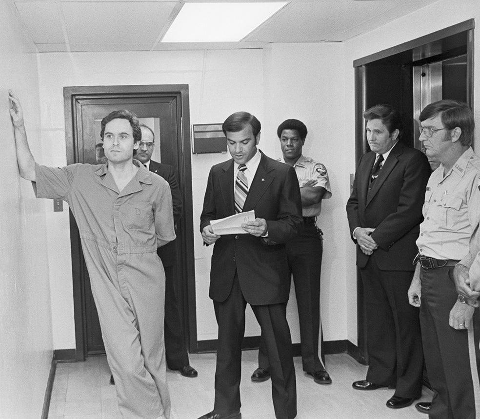 Ted Bundy, un hombre aparentemente encantador, confesó haber asesinado 30 mujeres después de una década negándolo. En la imagen, se apoya en la pared de la cárcel mientras el alguacil le lee una acusación por el asesinato de dos de ellas, en 1978.