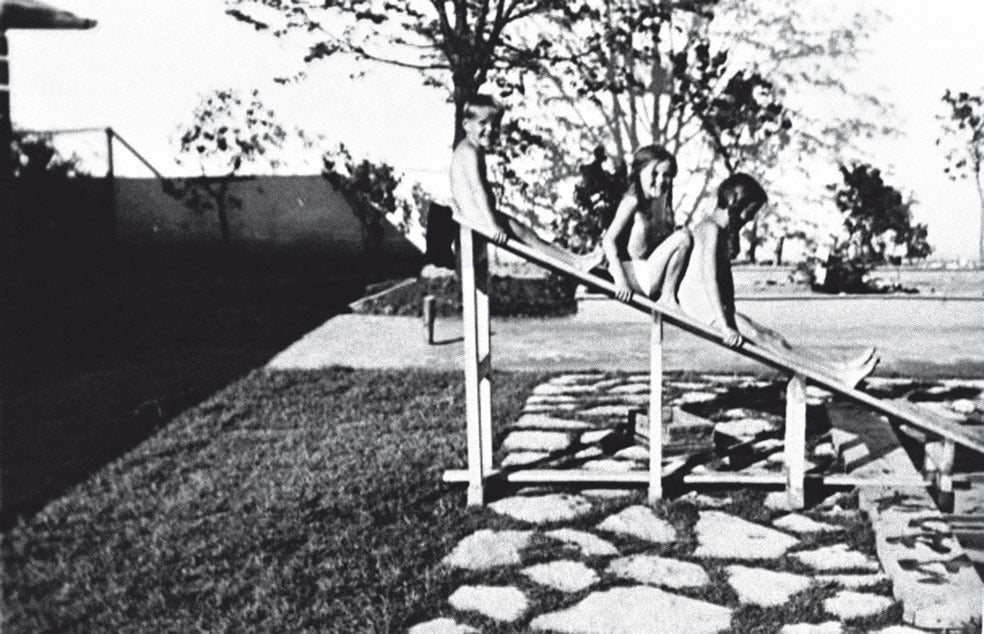 Brigitt jugaba con sus hermanos a «los deportados» a solo un centenar de metros de las cámaras de gas. En la imagen, Inge-Brigitt sentada entre Klaus y Heidetraud, en el tobogán de la casa de Auschwitz. Un muro al fondo separa el jardín del horror: el campo número uno, que el comandante mandó edificar en 1940.