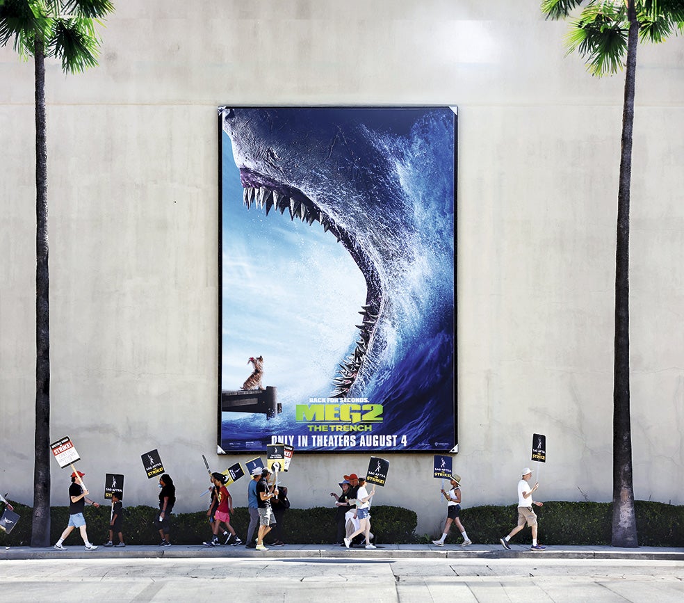 Escritores y actores de Estados Unidos protestan en Burbank, Los Ángeles, delante de un póster de la película Meg 2.