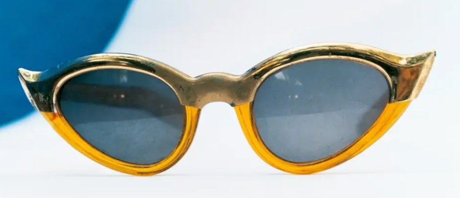 Estas gafas de sol amarillas de Frida Kahlo —un accesorio distintivo de la década del 50 que se observa en varias fotografías de la pintora mexicana— encapsulan su espíritu único y su estilo personal inconfundible hasta el punto de haberse convertido en un icono en sí mismas, un icono que aún hoy sigue inspirando colecciones completas de gafas de sol. El color amarillo vibrante refleja, a su vez, su inclinación por los colores vivos, la vitalidad con la que afrontó todas las adversidades y su habilidad para transformar lo ordinario en algo extraordinario. El auténtico don de su realismo mágico. Un modo único de mirar la vida.