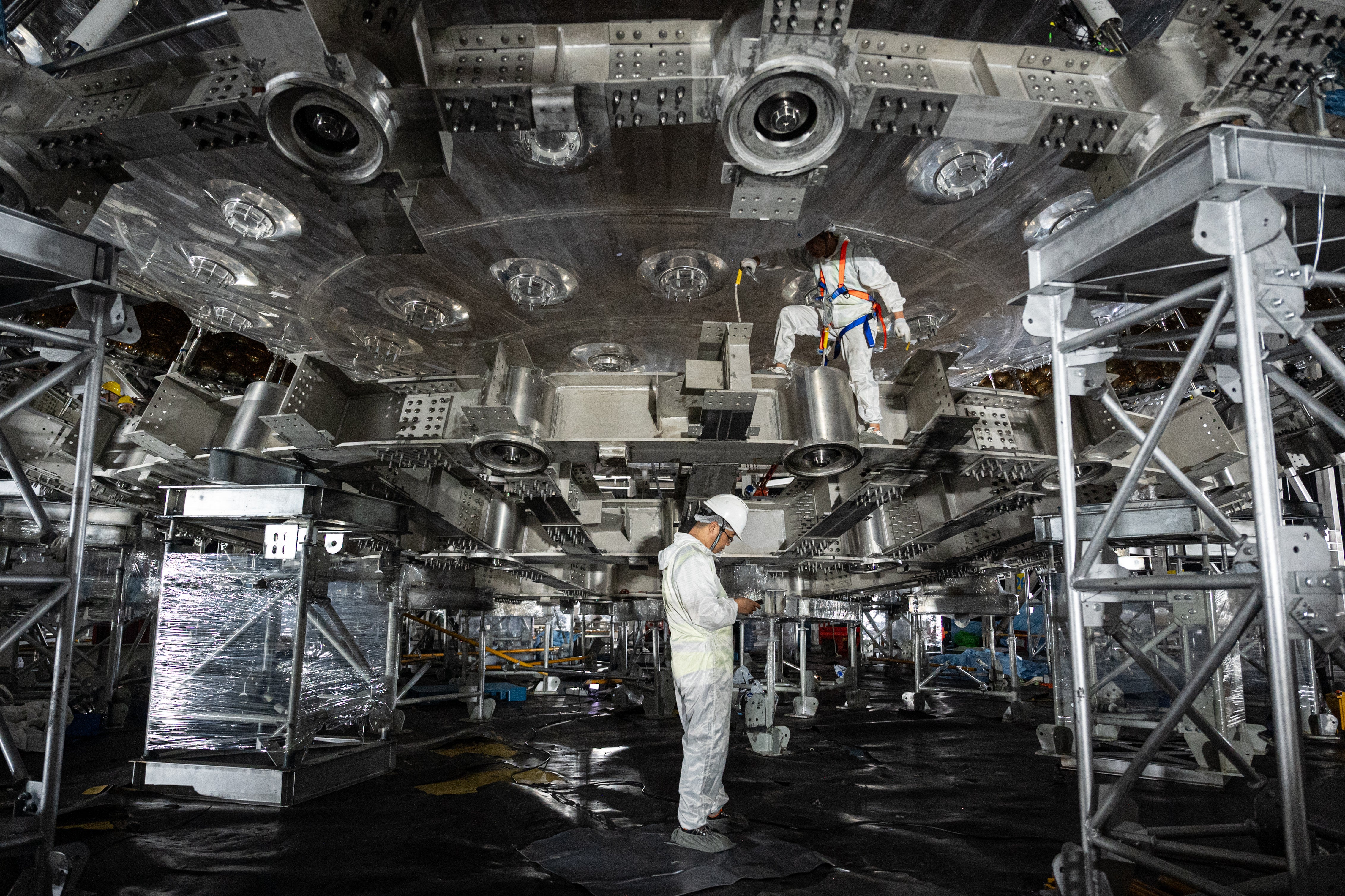 Empleados del el Observatorio Subterráneo de Neutrinos de Jiangmen trabajan en la estructura del detector de neutrinos, la esfera de 35 metros de diámetro, pieza central de las instalaciones.