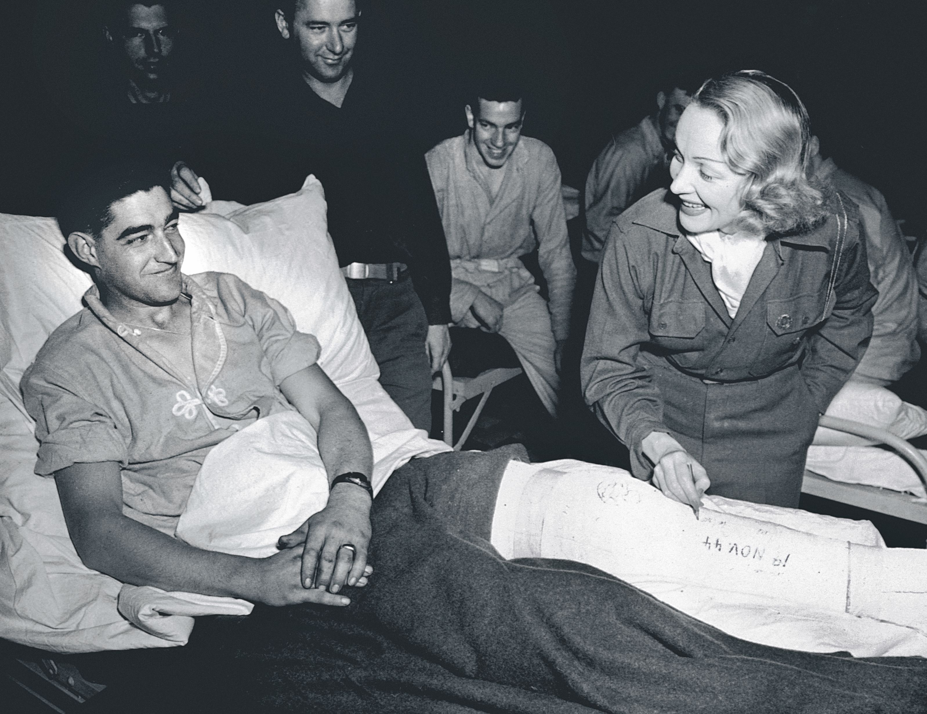 La actriz Marlene Dietrich escribiendo un autógrafo en la pierna escayolada de un herido en un hospital de campaña en Bélgica en noviembre de 1944.