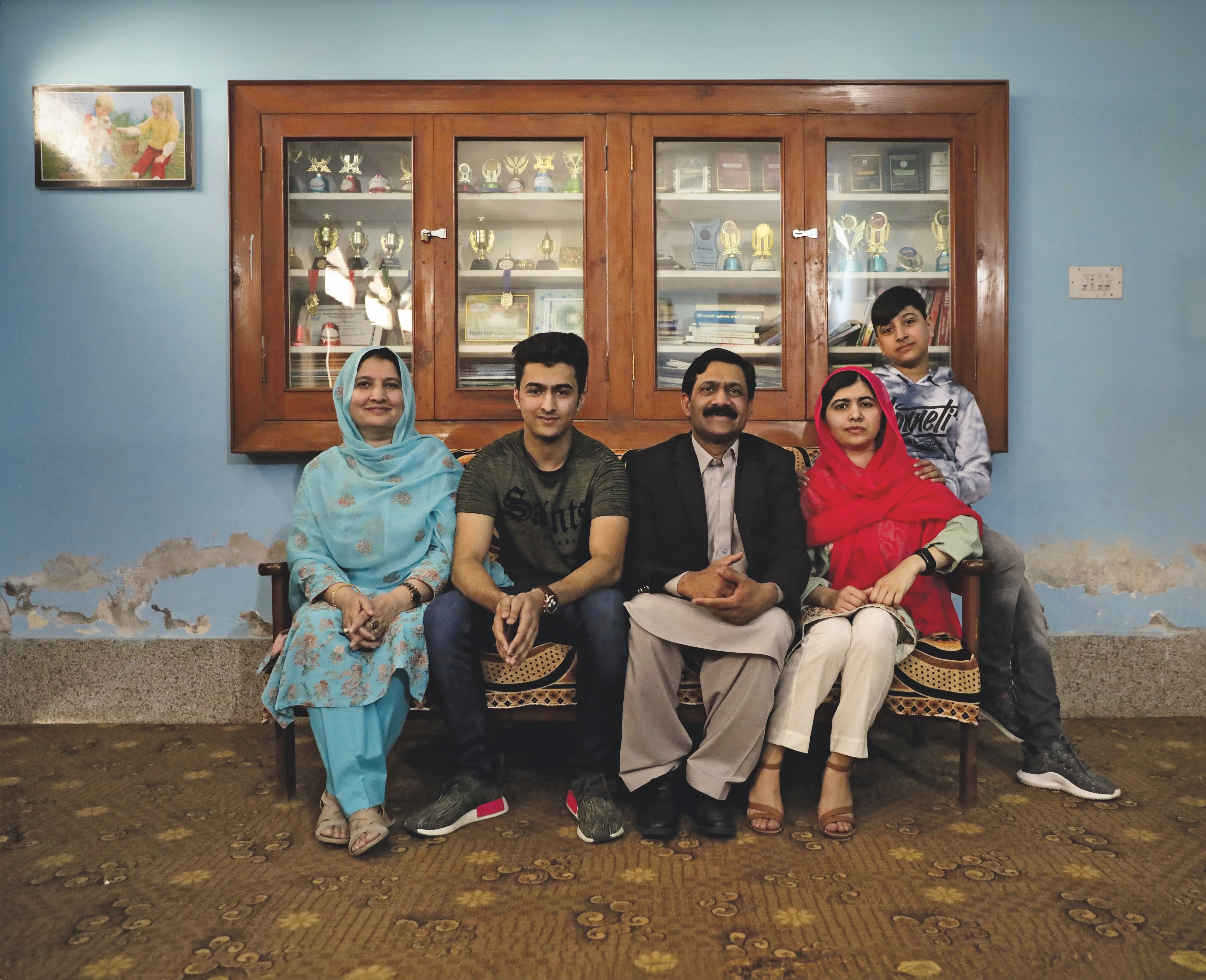 Malala con sus padres y sus hermanos en la habitación de su infancia en Pakistán, con los premios que ganó por sus logros académicos.